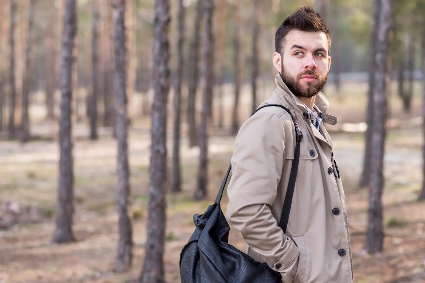 Gutaussehender männlicher Reisender mit einem Rucksack auf der Schulter, der wegschaut.