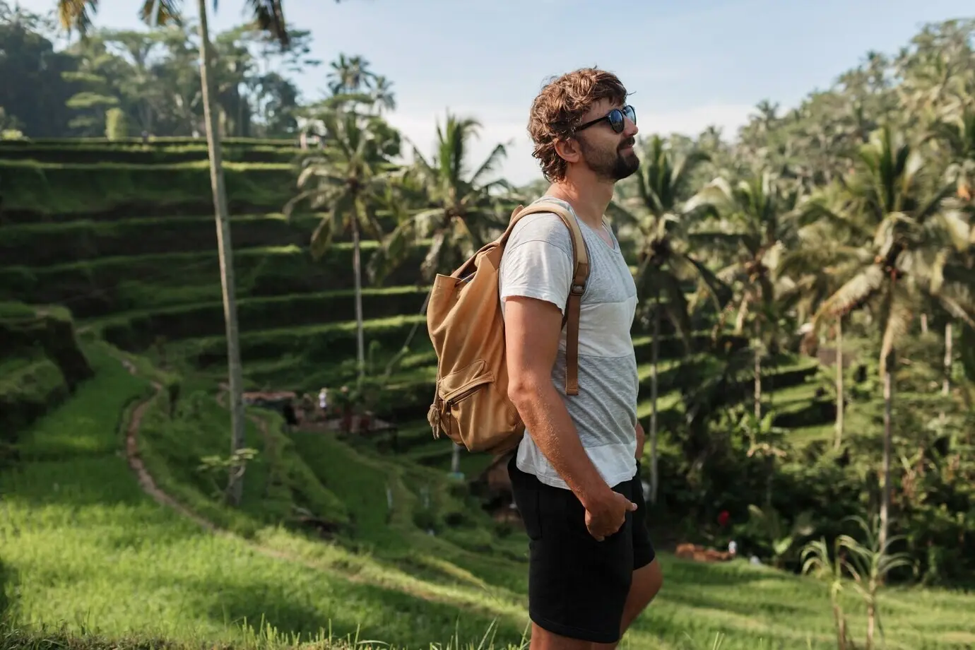Freiluftporträt eines gutaussehenden Reisenden mit Rucksack, der über eine Reisterrasse auf Bali läuft.